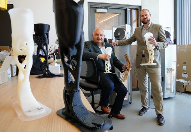 Two men in suits pose with 3-D printed prosthetic legs.