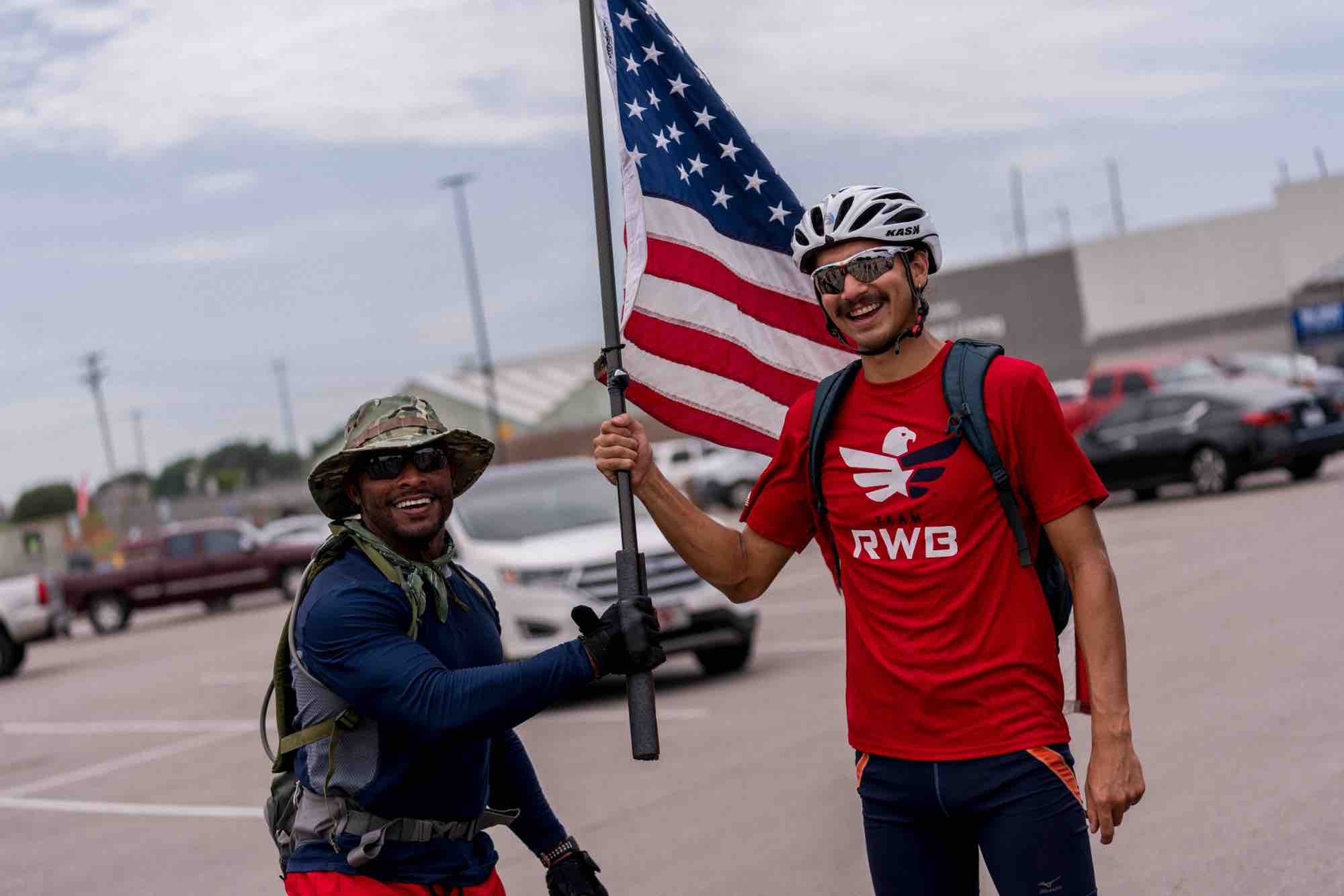 Two male veterans smile while passing the American Flag.