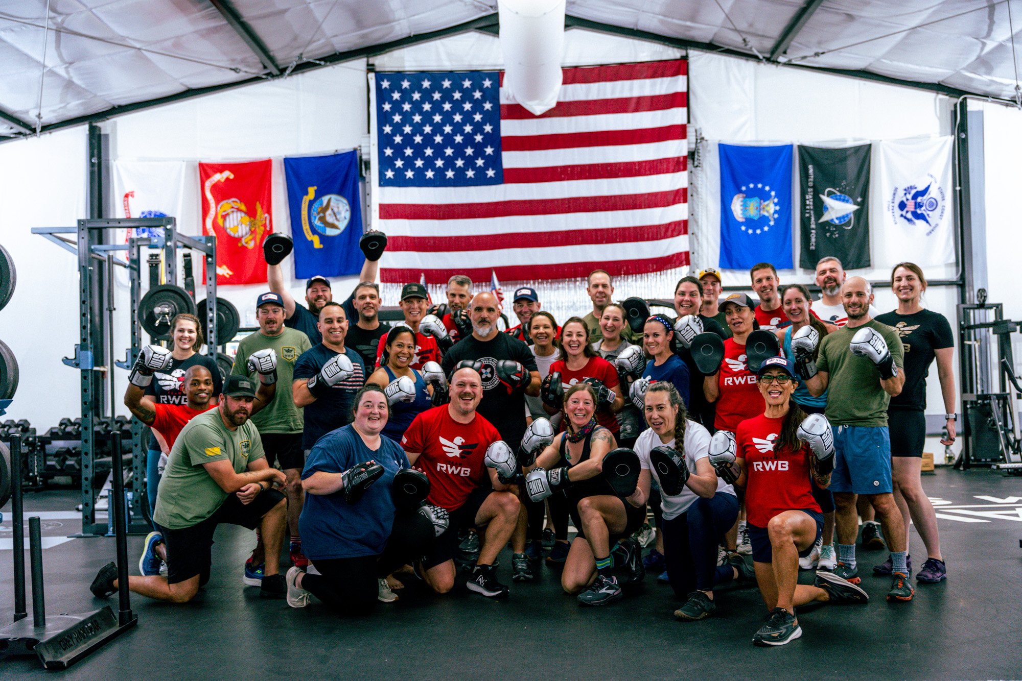 Team RWB staff standing in front of the American flag and all branch flags inside a gyme.