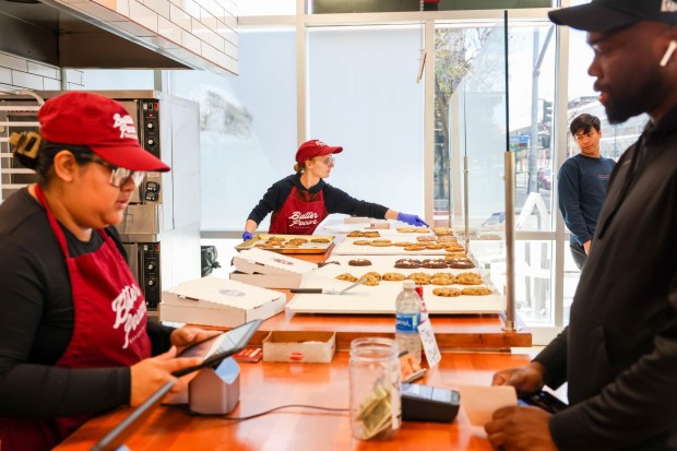 Crew members Aimee Martinez, left, helps a customer as Amber Hughes puts a variety of fresh cookies just baked at Butter Pecan Bakeshop in Emeryville, Calif., on Friday, April 12, 2024. (Ray Chavez/Bay Area News Group)