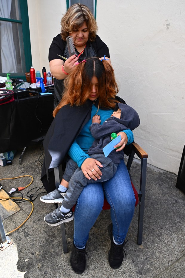 Paola Villanueva, of Soledad, holds her one-year old son Ulises as he sleeps while receiving a haircut from stylist Maria Gonzalez during the Farmworker Caravan Conference and Retreat held at the Saint Francis Retreat Center in San Juan Bautista, Calif., on Sunday, May 19, 2024. Over 50 stylists, barbers and make up artists will gathered today to treat farmworkers to make overs, offering a rare luxury to the largely low-income individuals. This week marks the second time that the event has been held. (Jose Carlos Fajardo/Bay Area News Group)