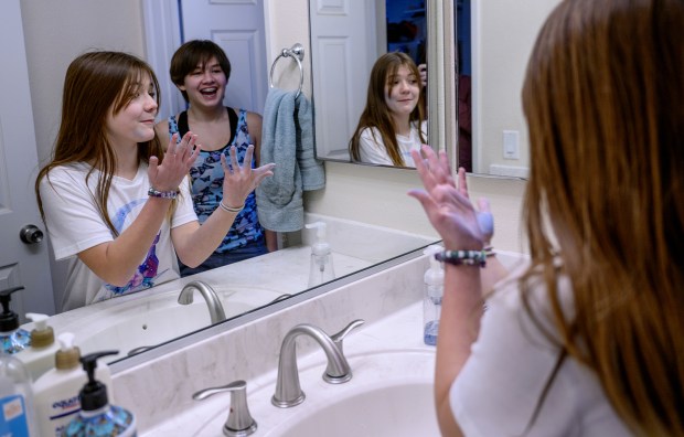 Rosie Wineman, 11, left, and Kestrel Wineman, 13, laugh while washing the colored chalk off their hands in the bathroom after making chalk drawings on their driveway. (Gina Ferazzi/Los Angeles Times/TNS)